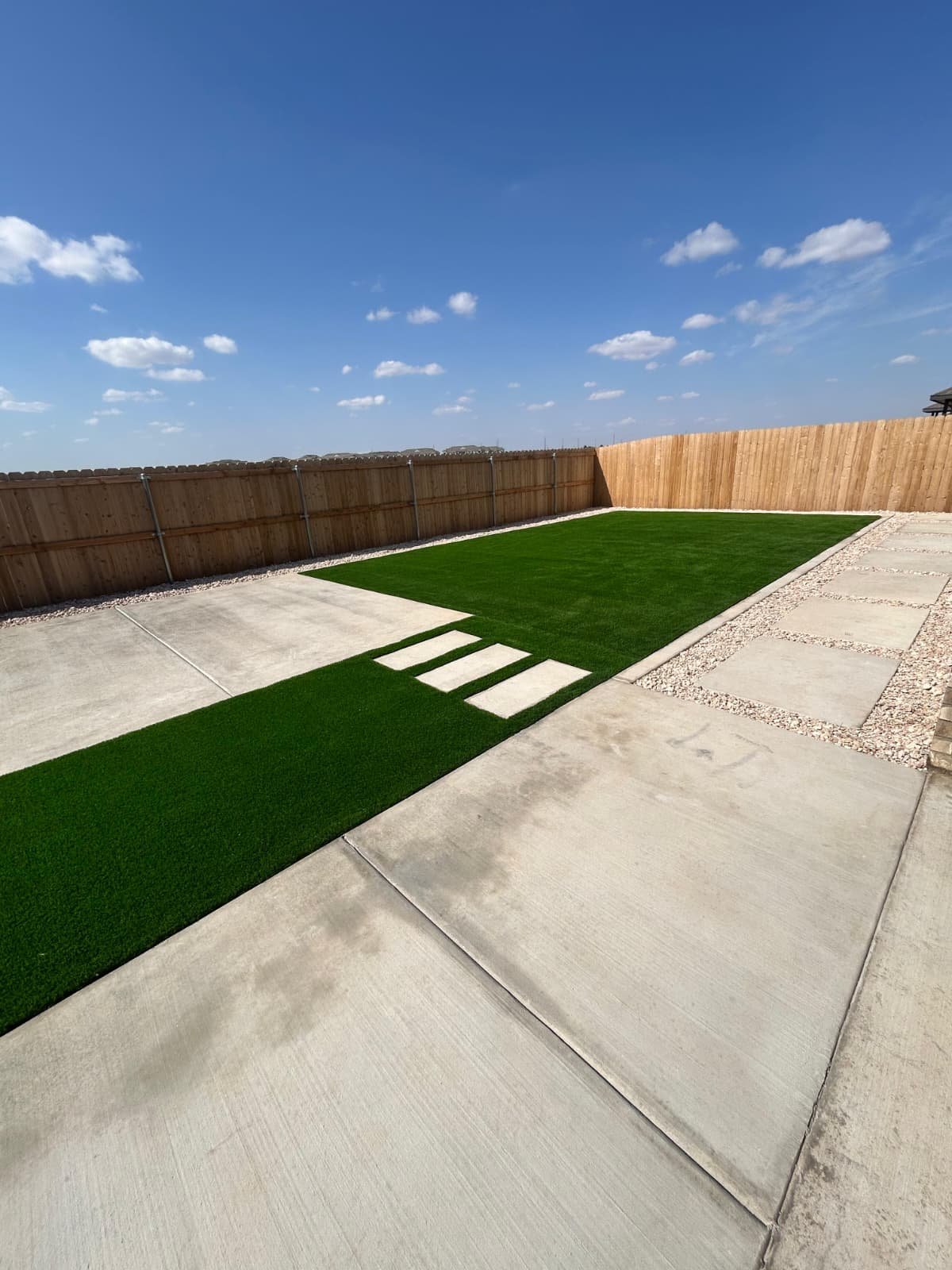 Backyard with artificial grass, a white stone path, and a gray stone border, featuring a pergola.
